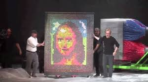 The finished result: a canvas rendered as the Mona Lisa entirely out of splattered paintballs, with three people standing beside it for scale.
